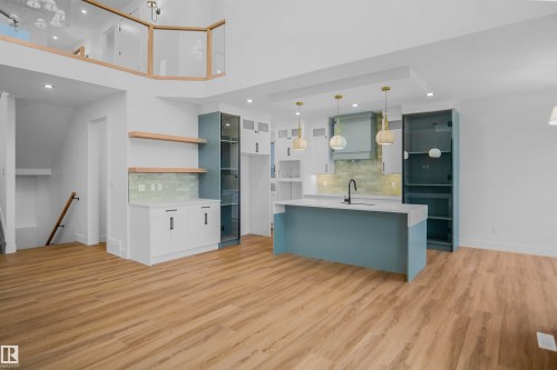 Open-concept living area with wood-finish flooring, a contemporary kitchen island with a sink and pendant lighting, and a kitchen featuring a light blue tile backsplash - 142 Edgewater Circle, Leduc, AB 