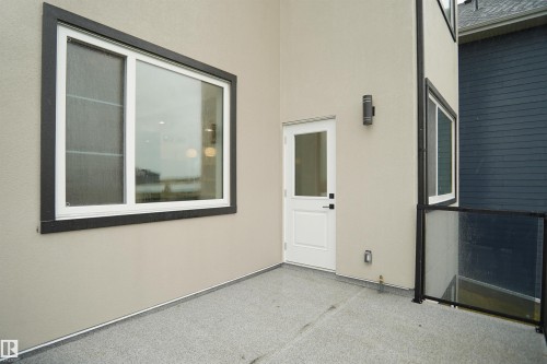 Outdoor patio area featuring a white door, large window with dark trim, and a glass railing - 142 Edgewater Circle, Leduc, AB 