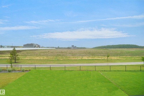 Expansive green lawn with a black metal fence, bordering a paved road and open fields - 142 Edgewater Circle, Leduc, AB 