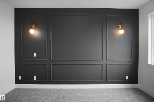 Accent wall featuring dark paneling with decorative trim, two wall-mounted sconces with spherical glass shades, and light gray carpeting - 142 Edgewater Circle, Leduc, AB 