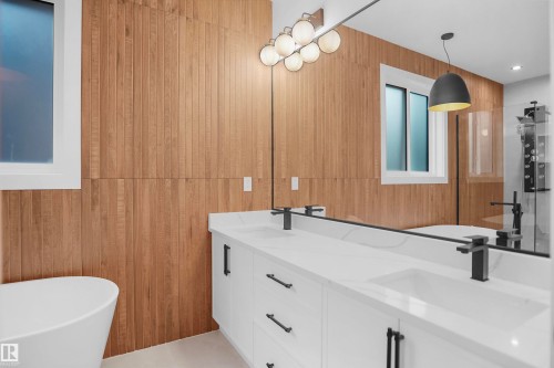 Modern bathroom featuring a double vanity with white cabinetry and integrated sinks, matte black fixtures, a white freestanding soaking tub, and vertical wood-finish wall paneling - 142 Edgewater Circle, Leduc, AB 