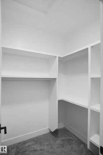 Walk-in closet featuring white built-in shelving, hanging rods, and gray carpeting - 142 Edgewater Circle, Leduc, AB 