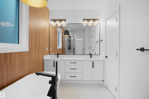 Contemporary bathroom featuring a freestanding tub with a matte black floor-mounted faucet, a double vanity with white cabinetry and integrated sinks, a large framed mirror, and a wood-slat accent wall - 142 Edgewater Circle, Leduc, AB 