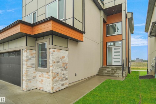 Contemporary exterior featuring a modern entry door with frosted glass panels, stone veneer accents, wood-finish siding, and a two-car garage - 142 Edgewater Circle, Leduc, AB 