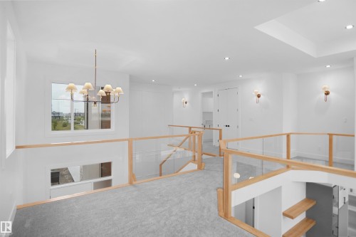 Upper-level landing featuring light gray carpeting, clear glass railings with wood-finish tops, a prominent ceiling-mounted chandelier, recessed lighting, and wall sconces - 142 Edgewater Circle, Leduc, AB 