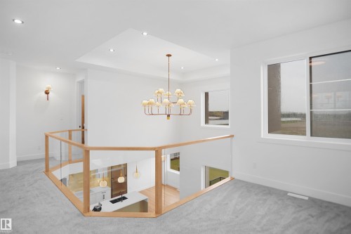 Open upper-level landing featuring light wood and glass railing, contemporary chandelier, recessed lighting, and wall sconces - 142 Edgewater Circle, Leduc, AB 