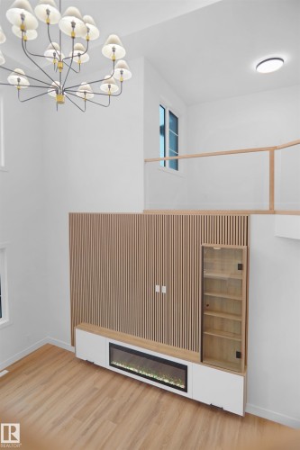 Open-concept interior featuring light wood-finish flooring, a contemporary chandelier, and a built-in media console with an integrated fireplace - 142 Edgewater Circle, Leduc, AB 
