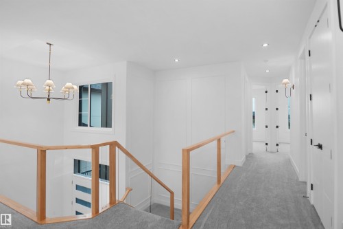 Upper landing featuring a contemporary chandelier, recessed lighting, glass panel railings with wood handrails, and panel molding on walls - 142 Edgewater Circle, Leduc, AB 