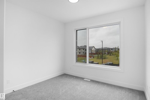 Interior room featuring a large window, light gray carpeting, white walls, white baseboards, and a ceiling-mounted light fixture - 142 Edgewater Circle, Leduc, AB 