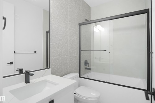 Bathroom featuring a tub/shower combination with black-framed glass sliding doors, a vanity with an integrated sink, a large mirror, and matte black fixtures - 142 Edgewater Circle, Leduc, AB 