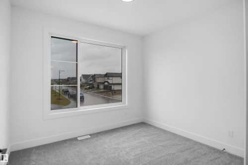 Bright room featuring a large window, neutral gray carpeting, white baseboards, and white painted walls - 142 Edgewater Circle, Leduc, AB 