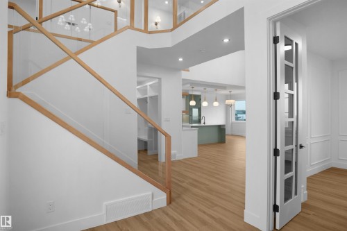 Open-concept interior featuring wood-finish flooring, a modern staircase with glass panels and wood handrails, recessed lighting, and a kitchen island with pendant lighting - 142 Edgewater Circle, Leduc, AB 