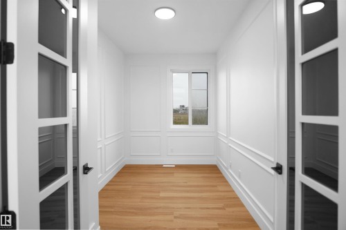 French doors with black hardware open to a room featuring light wood-finish flooring, white paneled walls, and a recessed ceiling light - 142 Edgewater Circle, Leduc, AB 