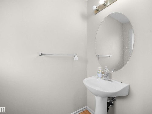 Pedestal sink with chrome faucet, oval wall mirror, and brushed nickel light fixture - 8111 7 Ave Avenue Sw, Edmonton, AB 