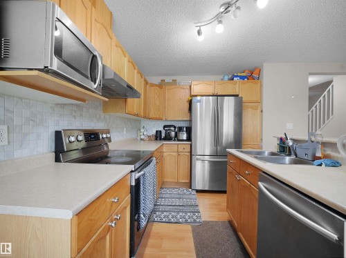 Kitchen featuring light wood cabinetry, stainless steel appliances, a tile backsplash, light-toned countertops, and wood-finish flooring - 8111 7 Ave Avenue Sw, Edmonton, AB 