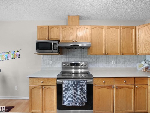 Kitchen featuring stainless steel appliances, wood cabinetry, light countertops, and a tiled backsplash - 8111 7 Ave Avenue Sw, Edmonton, AB 