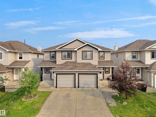 Duplex residence featuring light-toned siding, dark trim accents, a two-car attached garage, and a concrete driveway - 8111 7 Ave Avenue Sw, Edmonton, AB 