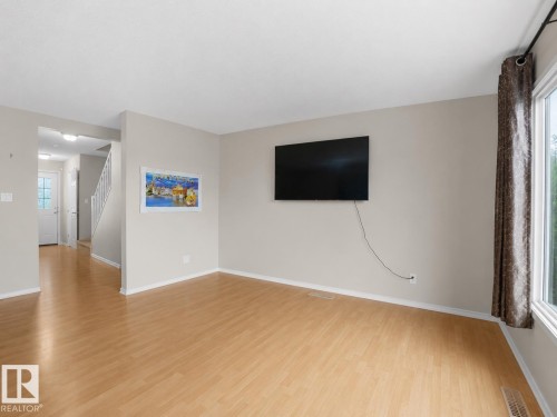 Light wood-finish flooring, neutral wall paint, and a bright window with a curtain rod - 8111 7 Ave Avenue Sw, Edmonton, AB 