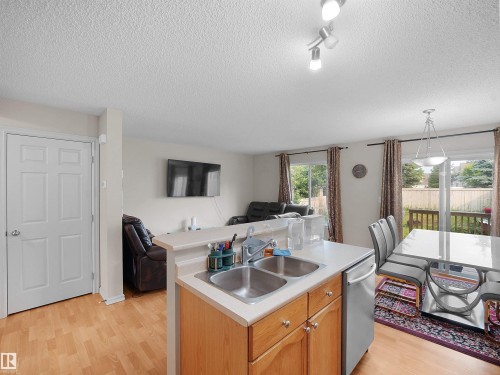 Kitchen featuring wood-finish cabinetry, stainless steel double sink, and a dishwasher - 8111 7 Ave Avenue Sw, Edmonton, AB 