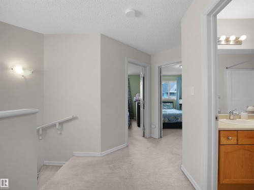 Carpeted hallway with painted walls, multiple doorways, and a bathroom vanity with a light wood-finish cabinet and built-in sink - 8111 7 Ave Avenue Sw, Edmonton, AB 