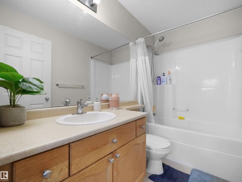 Bathroom featuring a wood-finish vanity with an integrated sink, a full-width mirror, and a shower-tub combination with a white surround - 8111 7 Ave Avenue Sw, Edmonton, AB 