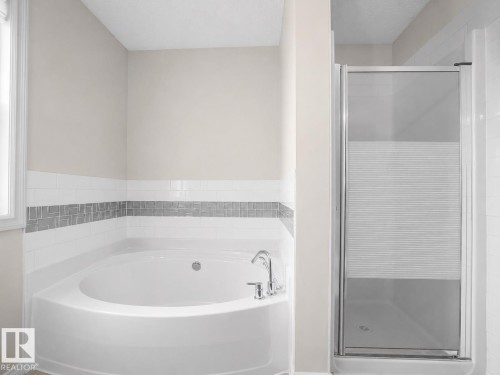 Corner soaking tub with polished chrome fixtures, subway tile surround, mosaic tile accent band, and separate shower with textured glass door - 8111 7 Ave Avenue Sw, Edmonton, AB 