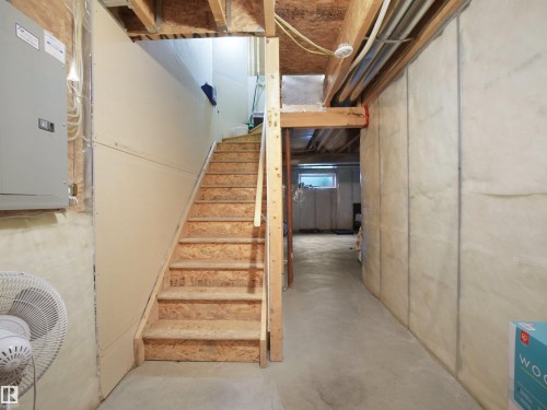 Unfinished basement with concrete flooring, exposed wood framing, and wood stairs - 8111 7 Ave Avenue Sw, Edmonton, AB 