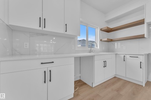 Modern kitchen with white cabinetry, light countertops, a stainless steel sink, wood-finish flooring, and open shelving - 285 Munn Way, Leduc, AB 