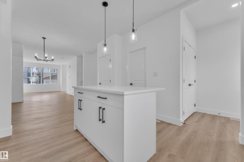 White kitchen island with a light-toned countertop, pendant lighting, and wood-finish flooring throughout - 285 Munn Way, Leduc, AB 