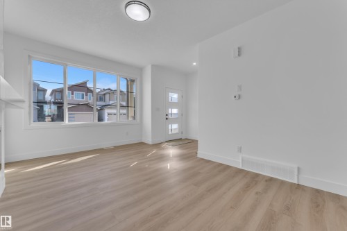 Spacious interior featuring a large multi-pane window, wood-finish flooring, white trim, and a contemporary entry door with frosted glass panels - 285 Munn Way, Leduc, AB 