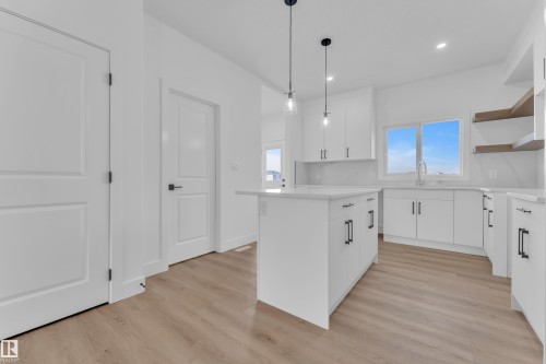 Kitchen featuring a central island with pendant lighting, white cabinetry with black hardware, light-toned wood-finish flooring, and open shelving - 285 Munn Way, Leduc, AB 