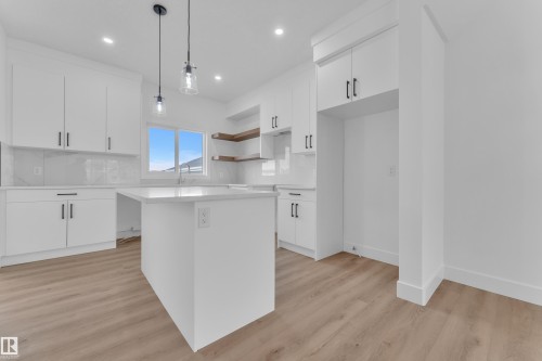 White kitchen featuring a central island, recessed lighting, wood-finish flooring, white cabinetry with dark hardware, and floating wood shelves - 285 Munn Way, Leduc, AB 