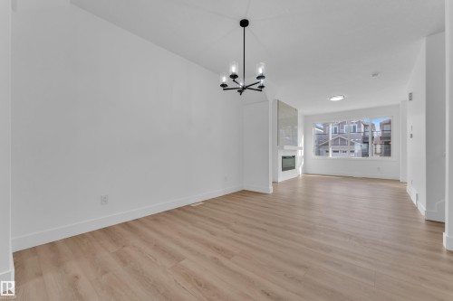 Open-concept living area featuring wood-finish flooring, a modern chandelier, and a built-in fireplace with a reflective surround - 285 Munn Way, Leduc, AB 