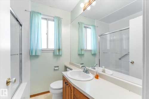Bathroom featuring a built-in wood-finish vanity with an integrated sink, a large wall mirror, and an enclosed shower - 9315 86 Street Nw, Edmonton, AB 