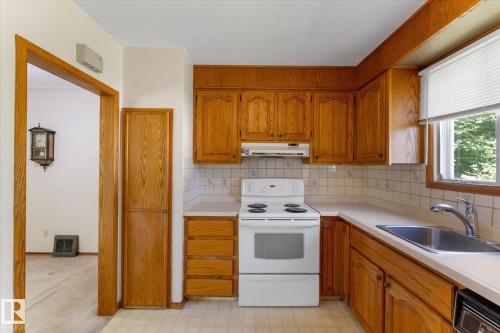Kitchen featuring wood cabinetry, solid surface countertops, tile backsplash, stainless steel sink, and white appliances - 9315 86 Street Nw, Edmonton, AB 
