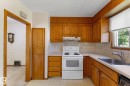 Kitchen featuring wood cabinetry, solid surface countertops, tile backsplash, stainless steel sink, and white appliances - 9315 86 Street Nw, Edmonton, AB 