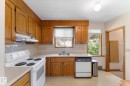 Kitchen featuring wood cabinetry, white tile backsplash, white countertops, and a stainless steel sink with a window above - 9315 86 Street Nw, Edmonton, AB 