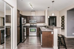 Kitchen featuring wood-finish flooring, stainless steel appliances, dark cabinetry, and a peninsula with a breakfast bar - 