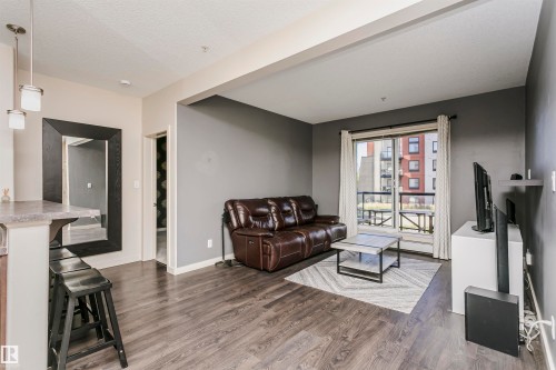 Spacious living area featuring wood-finish flooring and a sliding glass door to a private balcony - #217 304 Ambleside Link Sw, Edmonton, AB 