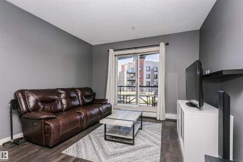 Dark wood-finish flooring, neutral gray wall paint, and a sliding glass door with a balcony - #217 304 Ambleside Link Sw, Edmonton, AB 