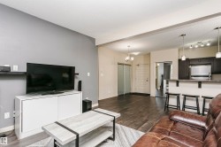 Spacious living area featuring wood-finish flooring, recessed lighting, and a modern kitchen with a breakfast bar and stainless steel appliances - 