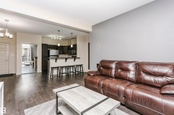 Open-concept living area featuring wood-finish flooring, a kitchen with dark cabinetry, stainless steel appliances, and a breakfast bar - 