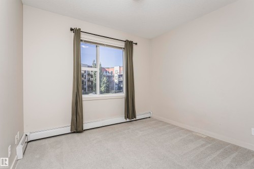 Carpeted flooring, neutral wall color, window with exterior building and tree scenery, baseboard heating elements - #217 304 Ambleside Link Sw, Edmonton, AB 