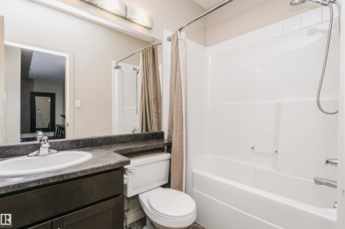 Bathroom featuring a dark wood-finish vanity with an integrated sink, a dark countertop, and a white bathtub with a shower - #217 304 Ambleside Link Sw, Edmonton, AB 