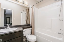 Bathroom featuring a dark wood-finish vanity with an integrated sink, a dark countertop, and a white bathtub with a shower - 