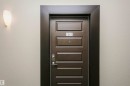 Paneled entry door with dark trim, featuring a wall-mounted sconce - #217 304 Ambleside Link Sw, Edmonton, AB 