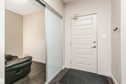 Entryway featuring a paneled door with brushed nickel hardware, wood-finish flooring, and a sliding frosted glass panel - #217 304 Ambleside Link Sw, Edmonton, AB 