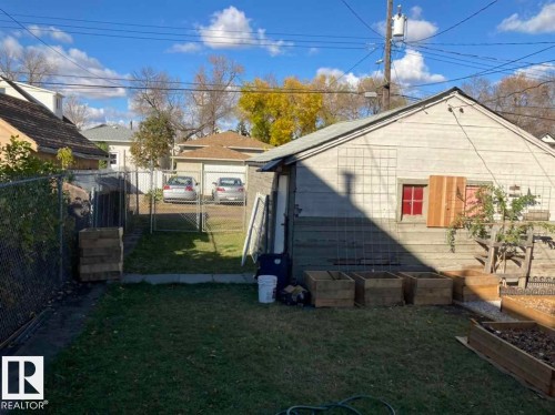 Expansive backyard featuring a chain-link fence, detached garage, and raised garden beds - 9332 106A Avenue Nw, Edmonton, AB 