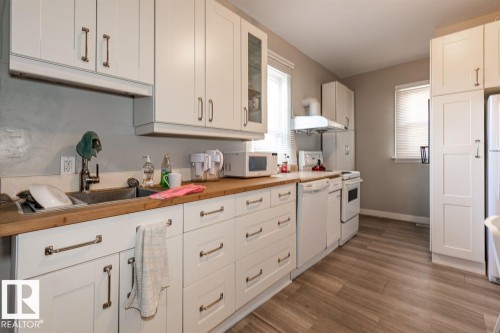 White shaker-style cabinetry with long pull hardware, wood-finish countertops, wood-finish flooring, undermount sink with a gooseneck faucet, and white appliances - 9332 106A Avenue Nw, Edmonton, AB 