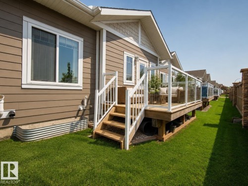 Private deck with glass panel railing and wooden stairs, set against a siding exterior with white window trim - #9 175 Mcconachie Dr Nw, Edmonton, AB 